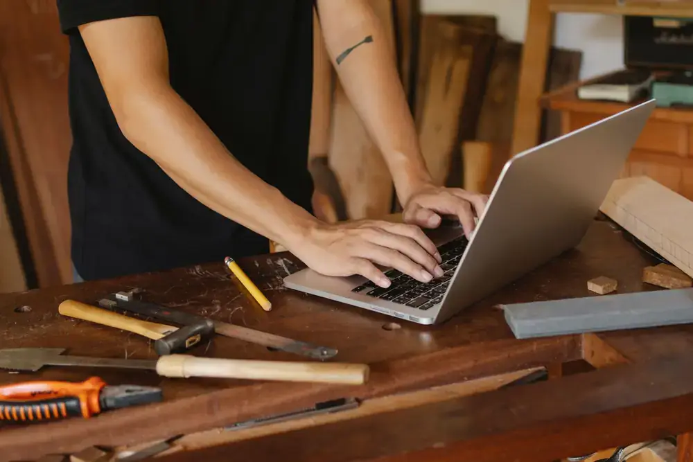 Hands typing on a laptop on a wooden workshop table